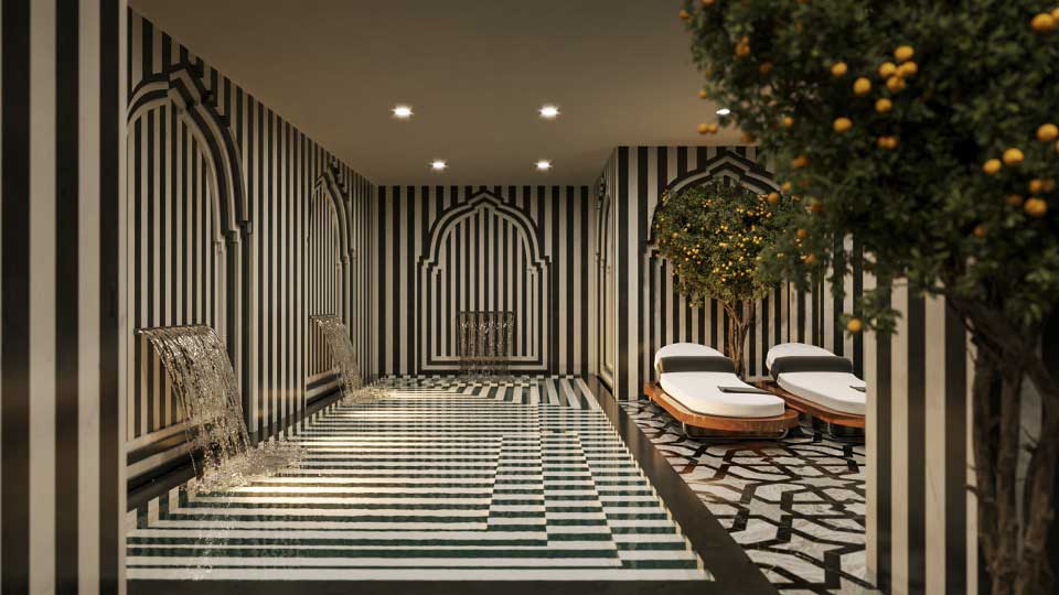 foto zona de aguas del spa del gran hotel Claridge granada. lleva un mosaico de marmol blanco y negro una piscina con dos cascadas de agua, dos tumbonas y un naranjo